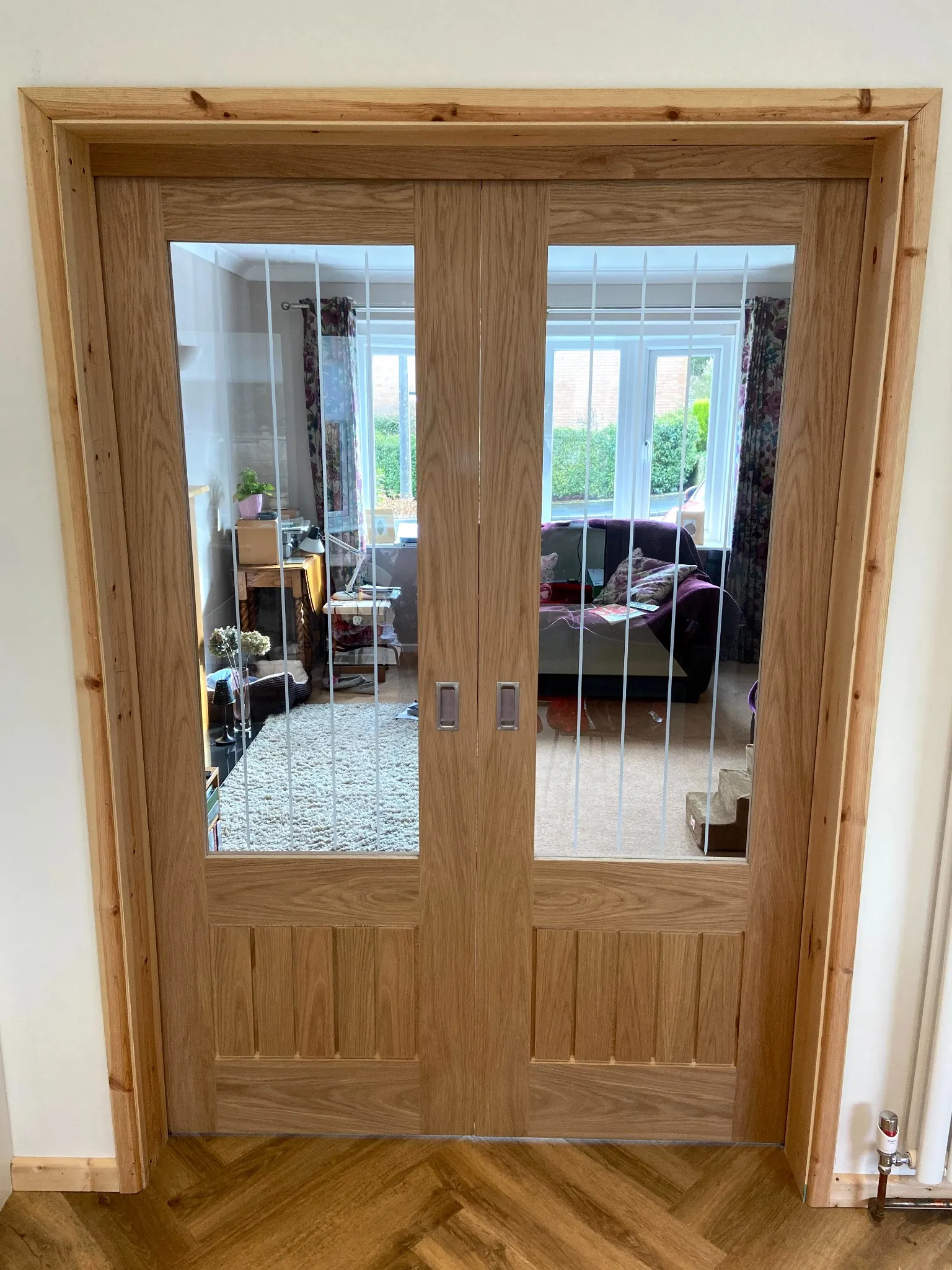 Bespoke oak double pocket doors with slim glass panels separating two living spaces in a Cheshire home.